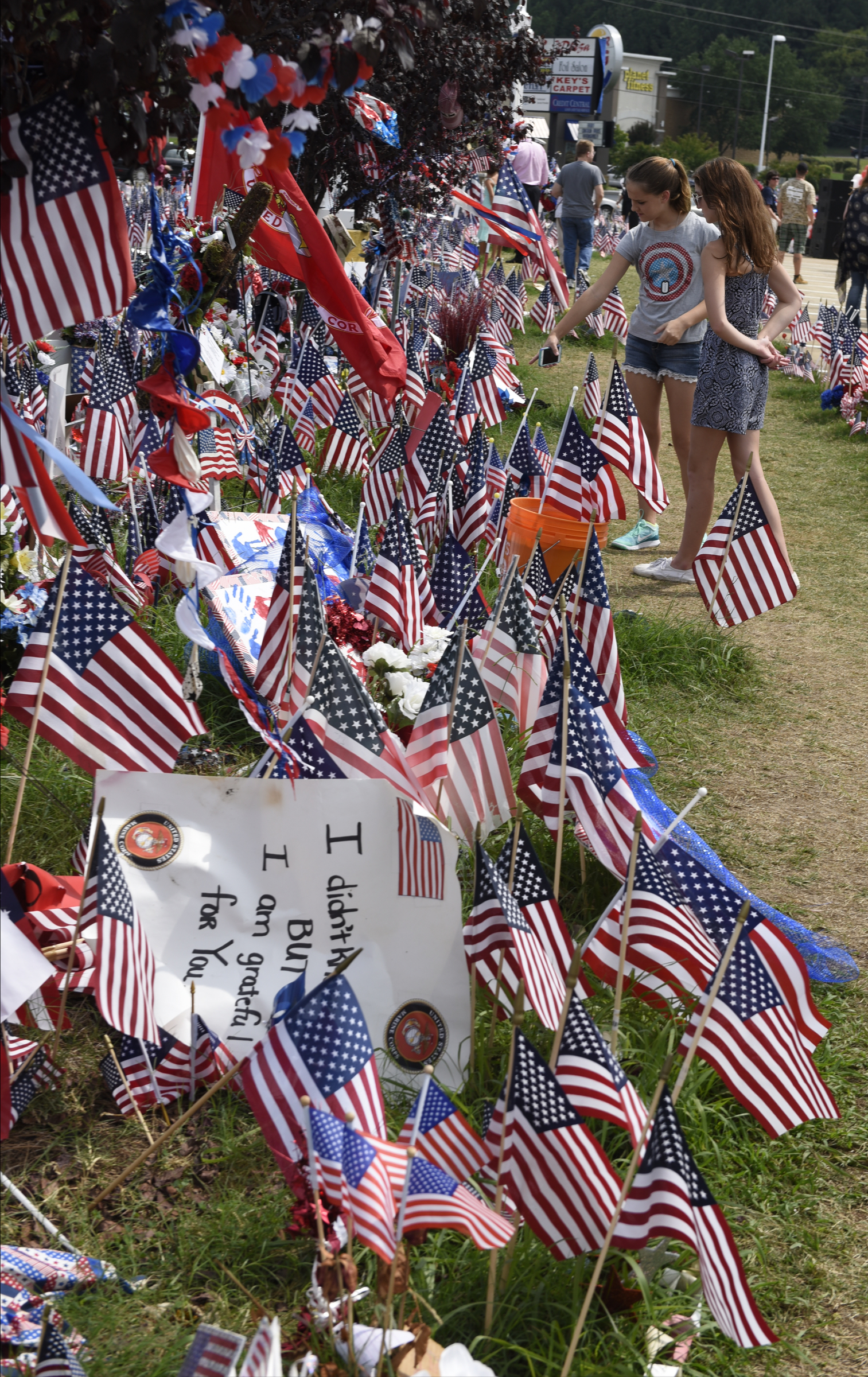 Sara Burhans, left, and Makenna Seitz look at a display of flags prior to an opening ceremony Sunday, Aug. 16, 2015, in Chattanooga, Tenn., at a memorial to the five servicemen who were killed on July 16. The memorial is located at 6219 Lee Highway near the Armed Forces Career Center where the July attack began.