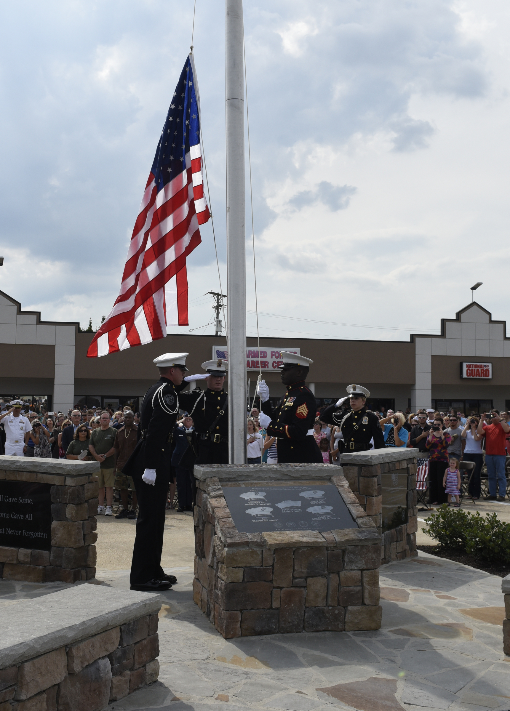U. S. Marine Sgt. Demonte Cheeley raises an American flag during an opening ceremony Sunday, Aug. 16, 2015, in Chattanooga, Tenn., at a memorial to the five servicemen who were killed on July 16. Sgt. Cheeley, who was wounded in the attack, is assisted by members of the Chattanooga Police Department Honor Guard, from left, Christopher Grafe, Lance Lockhart and Jamie Barrow. The memorial is located at 6219 Lee Highway near the Armed Forces Career Center where the July attack began.