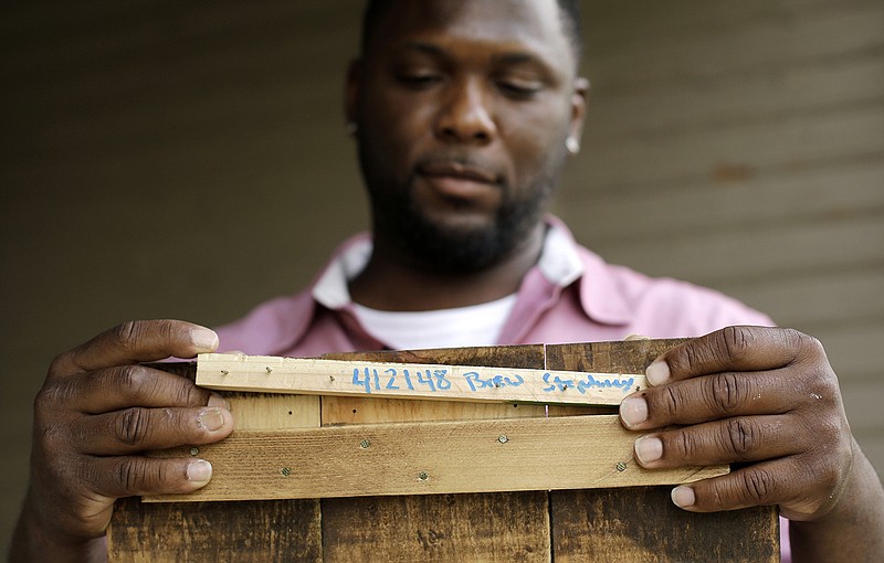 In this Aug. 14, 2015 photo, Larry Stephney holds a piece of wood with the number 412148 written on it that is from a product made while he was an inmate at a privately run prison in Nashville, Tenn. The number refers to a section of Tennessee code that makes it illegal for jail officials to require an inmate to perform labor that results in the official's personal gain. Stephney says inmates were required to build plaques, birdhouses, dog beds and cornhole games for officials who sold the items through an online business and at a local flea market.