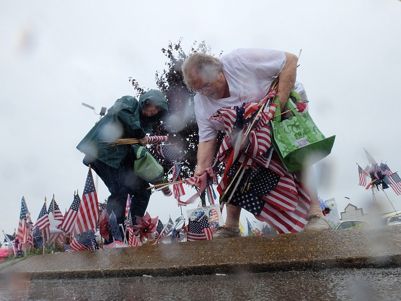Brenda Bailey, left, and Bette Cook gather flag and memorabilia in a downpour Monday at the makeshift memorial left by area residents at the Lee Highway shooting site near Highway 153.