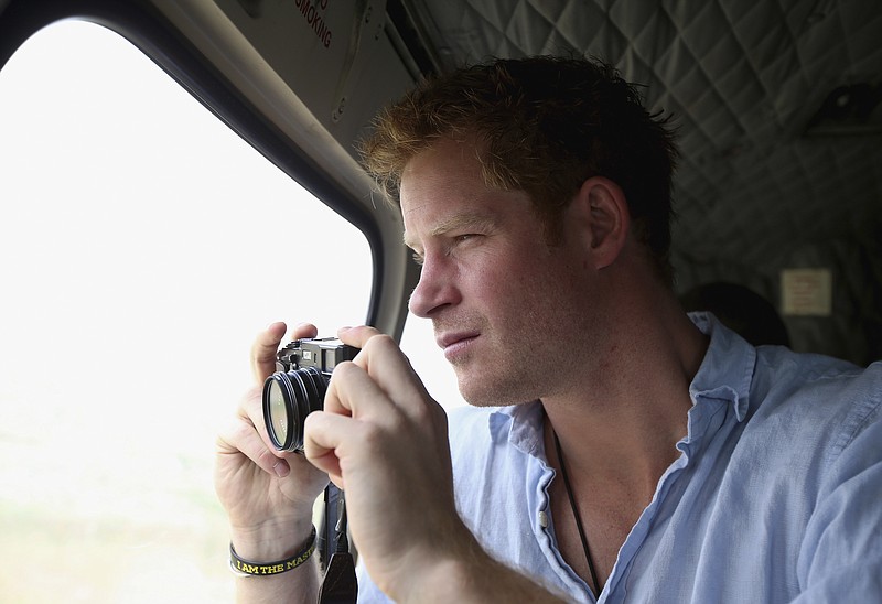 
              FILE - In this Dec 8, 2014, file photo, Prince Harry takes a photograph out of the window of a helicopter as he travels over the Muluti Mountains on his way to visit a herd boy night school constructed by his Sentebale charity, in Mokhotlong, Lesotho. Prince Harry has been on a private visit to Kruger National Park, South Africa's flagship wildlife park, where poachers have killed rhinos in record numbers and clashed with rangers, the service said in a statement emailed Thursday, Aug. 13, 2015, to The Associated Press. (Chris Jackson/Pool Photo via AP, File)
            