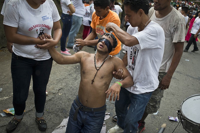
              In this Aug. 10, 2015 photo, a “promesante” or devotee of Managua's patron saint, Santo Domingo de Guzman, wearing a blindfold, advances on his knees towards the Las Sierritas parish church, while he is assisted relatives, as a payment for a perceived miracle performed by the saint, in Managua, Nicaragua. Devotees make the last 200 meters to the saint's altar in the Las Sierritas parish church on their knees. (AP Photo/Esteban Felix)
            