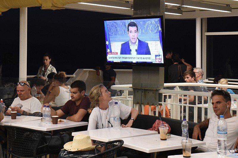 Greek Prime Minister Alexis Tsipras, on a screen during a televised address to the nation, as a tourist watches on a ferry traveling in the Aegean sea, near Syros island, Greece, on Thursday, Aug. 20, 2015.