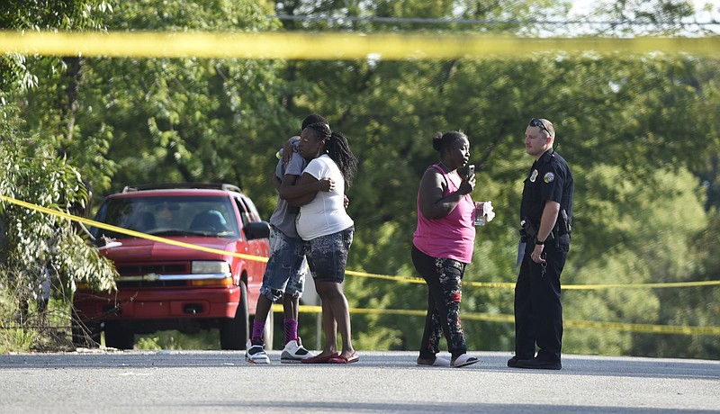 Two people embrace as a woman talks with a Chattanooga police officer following an afternoon shooting in the 3100 block of 7th Avenue on Sunday, Aug. 23, 2015, in Chattanooga that left a 14-year-old boy with gunshot wounds to his arm, leg and chest.