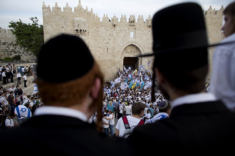 
              FILE - In this May 28, 2014, file photo, Ultra-Orthodox Jews watch people wave Israeli flags outside the Old City's Damascus Gate during Jerusalem Day celebrations in Jerusalem. A recent demonstration by ultra-Orthodox Jews against a new cinema opening its doors on the Sabbath was meant to be a show of strength in a long-running battle over the role of strict Jewish law in the cultural life of Jerusalem. But in many ways, it was also a sign of desperation after a series of gains by the city’s secular community in recent years.  (AP Photo/Dusan Vranic, File)
            