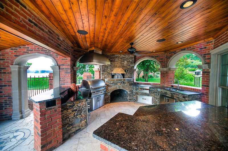 This outdoor kitchen, designed and built by Southern Hearth and Patio, has a grill, left, a fireplace, center, a griddle, right of the fireplace and a sink. Not to mention grainite countertops, a wooden ceiling and stone floors.