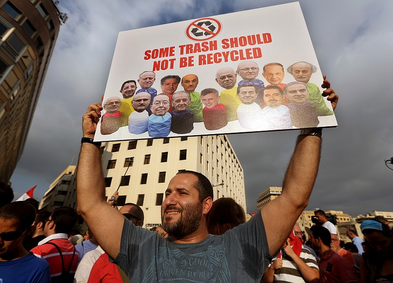 
              FILE -- In this August 22, file photo, a Lebanese activist holds a poster with pictures of Lebanese Cabinet ministers during a protest against the ongoing trash crisis, in downtown Beirut, Lebanon. To the casual visitor, Lebanon may look like a relative success story: a tiny slice of modernity and coexistence in a turbulent region plagued by violence and extremism _ but the reality is quite different. For residents, it’s a failed state  eaten away by a sectarian political class, and while recent trash protests have challenged that system, others argue it’s what’s allowed a country of 4.5 million people from 18 recognized sects to survive. (AP Photo/Bilal Hussein, File)
            