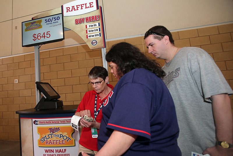 
              FILE -- In this May 27, 2014 file photo, Mary Saylor, left, sells a $5 raffle ticket to Erica and Jerry Oie prior to the Texas Rangers-Minnesota Twins baseball game, in Minneapolis. As hight-stakes charity raffles gain popularity at sports venues across the nation, California clubs and a leading raffle vendor are lobbying state lawmakers to authorize 50-50 raffles in California.  Critics call it an unfair exemption that favors franchise owners over food banks, PTAs and churches. (AP Photo/Jim Mone,file)
            