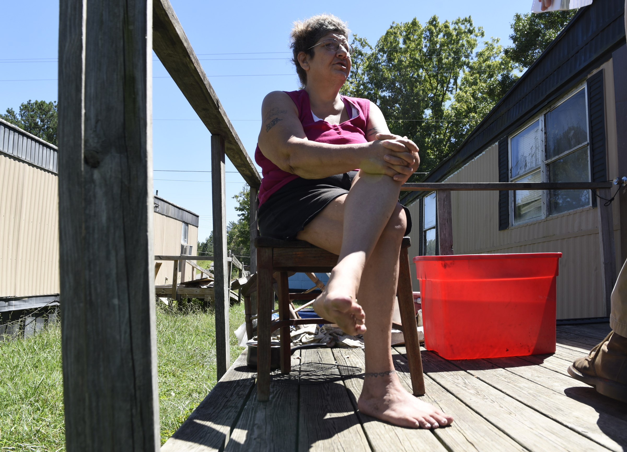 Nikki Cortez  sits next to a plastic tub filled with rain water on the deck of her residence at the Pear Pines Mobile Home Park on Tuesday, Aug. 25, 2015, in LaFayette, Ga. Few residents remain after the landlord's financial problems caused water to be turned off at the property several weeks ago.