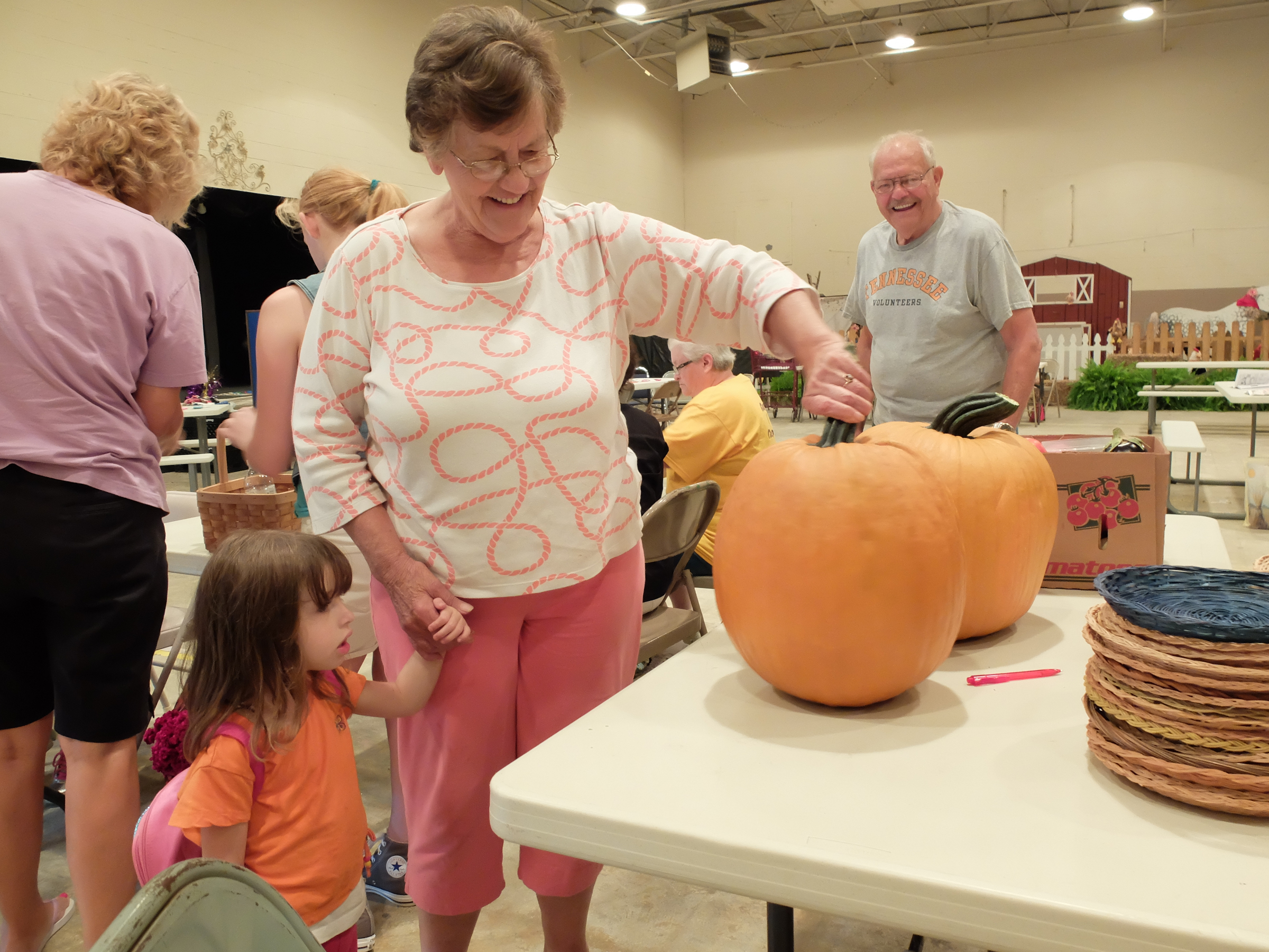 Little Rileigh Keener, 4, lower left, looks at the pumpkins grown by Mary Farley, center. Bill Lowe, right, smiles as they guess at the weight of the produce Monday during registration.  The 88th Annual Sequatchie County Fair opens Wednesday and runs through Monday, Sept. 7.