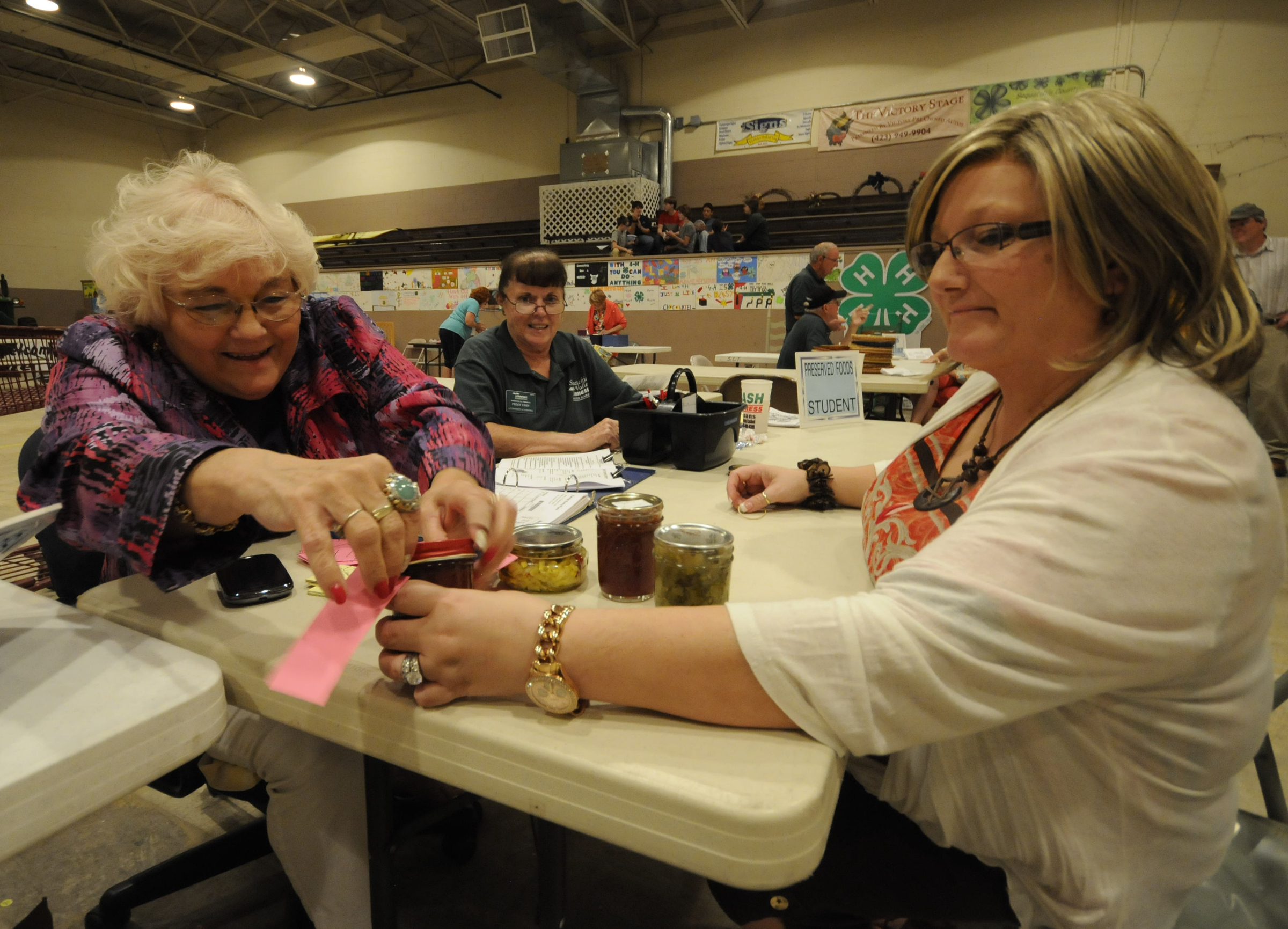 Sequatchie County Fair board member Sammye Finley, left, attaches a tag to Robin Burgin's, right, strawberry jam for judging Tuesday at the 88th Annual Sequatchie County Fair in Dunlap. Entries for the preserved food segment closed Monday at 7 p.m. Peggy Uhey, center, helps record the entries in the former gym of the Sequatchie County Middle School.