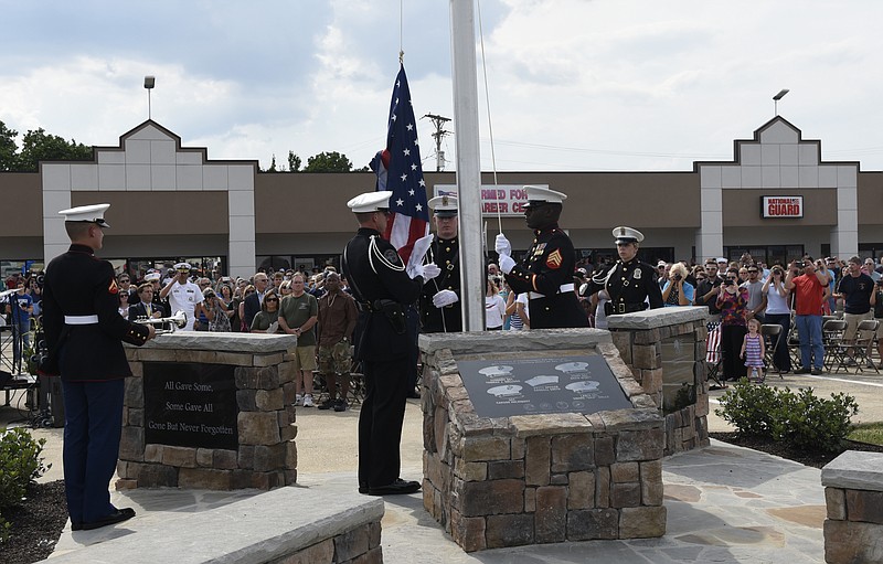 U. S. Marine Sgt. Demonte Cheeley raises an American flag during an opening ceremony Sunday, Aug. 16, 2015, in Chattanooga, Tenn., at a memorial to the five servicemen who were killed on July 16. Sgt. Cheeley, who was wounded in the attack, is assisted by members of the Chattanooga Police Department Honor Guard, from left, Christopher Grafe, Lance Lockhart and Jamie Barrow. At left is Marine Lance Cpl. James Draffen, who played "Taps" after the flag was raised. The memorial is located at 6219 Lee Highway near the Armed Forces Career Center where the July attack began. 