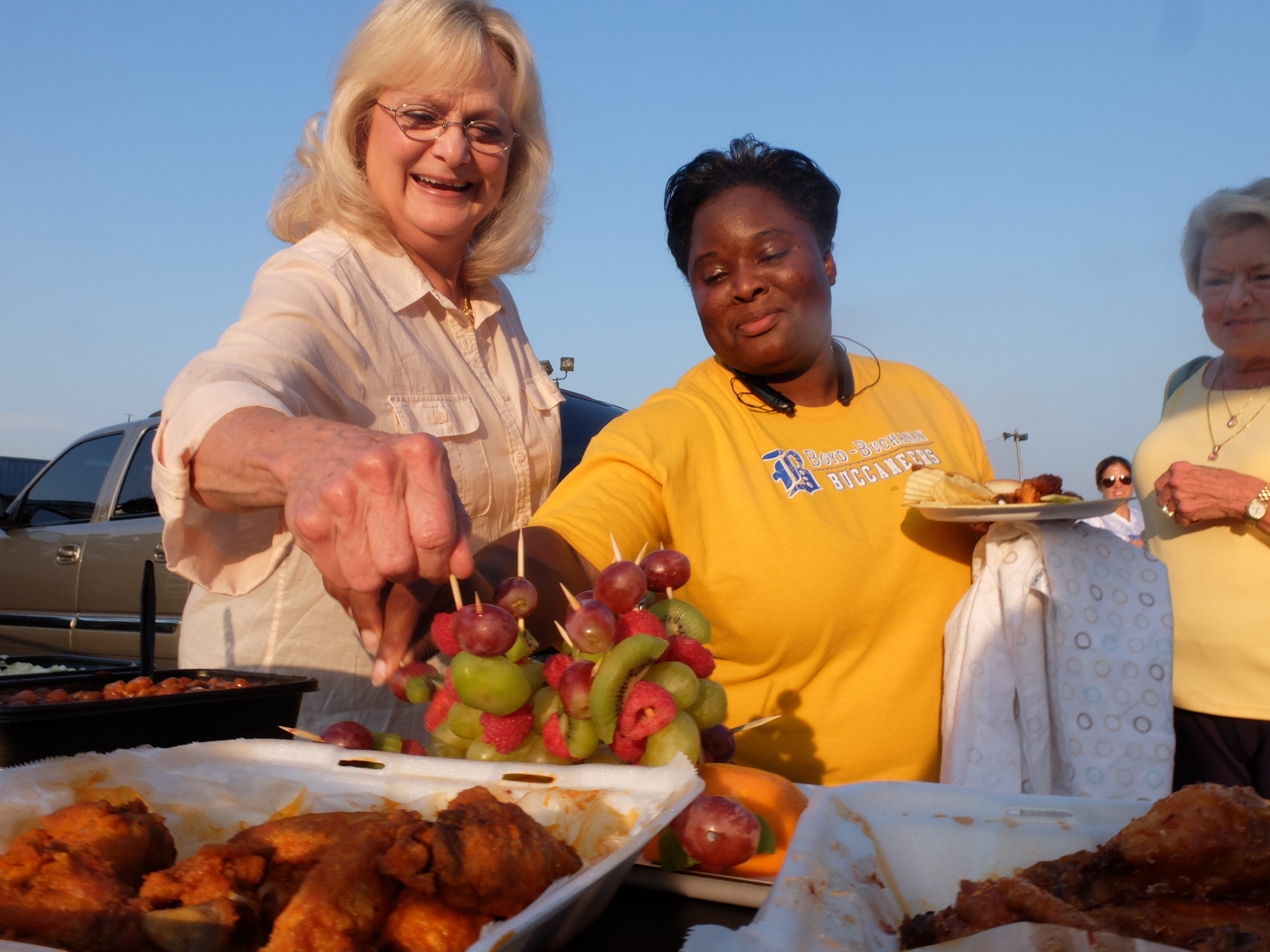 Boyd-Buchanan parent and grandparent fans Gaila Pettway, left, and Amanda Bailey reach for fruit while tailgating Friday night.