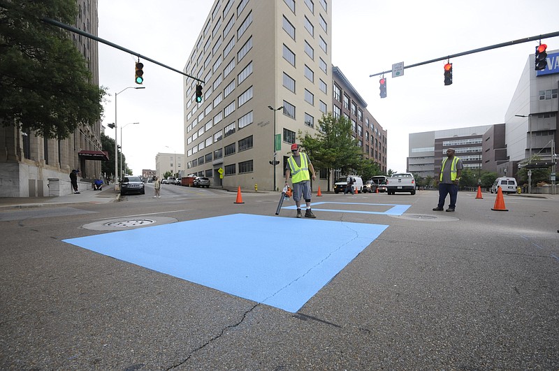 Eddie Poe uses a motorized blower to dry Innovation District logo paint in the middle of the intersection at Market and E. 11th Streets Wednesday morning. "This is a nine-square design to draw attention to Innovation District headquarters, " said Ben Taylor, CDOT assistant Transportation Engineer. The headquarters are to be located in the multi-story Edney Building across from Patten Towers.