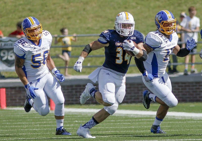 UTC running back Derrick Craine finds a hole between Mars Hill defenders Lane Burnett, left, and Trey Clark, right, during the Mocs' football game against the Lions at Finley Stadium on Saturday, Sept. 12, 2015, in Chattanooga, Tenn. UTC won 44-34.