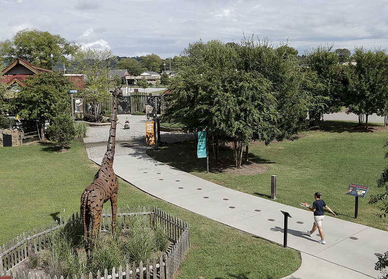 A staff member walks past a statue of a giraffe along a path that will be redesigned, with a lion enclosure to the left and giraffe enclosure to the right, at the Chattanooga Zoo on Thursday, Sept. 10, 2015, in Chattanooga, Tenn. The zoo has announced plans for a $10 million project to repurpose areas near the current entrance for a giraffe enclosure, scheduled to be completed in 2018, and a lion enclosure, scheduled for completion in 2020.