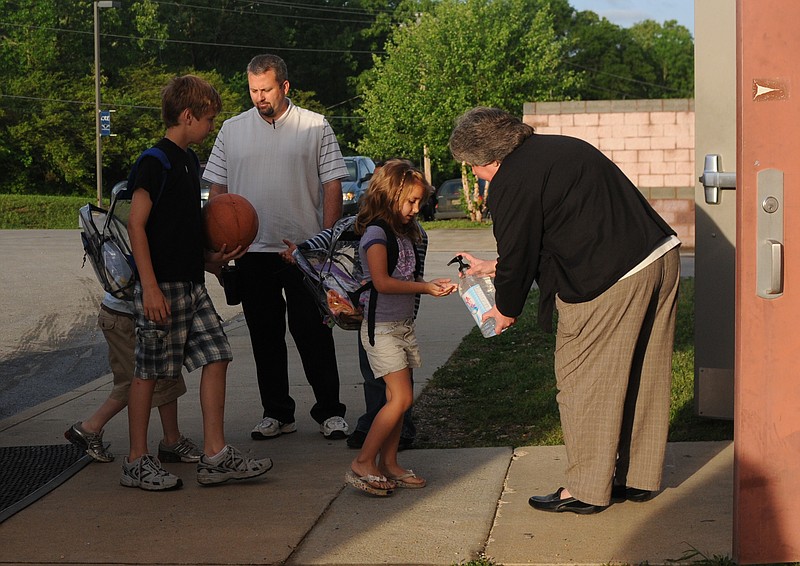 Students at Cherokee Ridge Elementary are met at the door by assistant principal Tom Langford and principal Lori Vann, far right, who is dispensing hand sanitizer before the children enter the building.