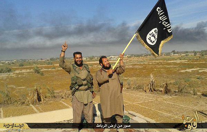 In this photo released on Sunday, June 28, 2015, by a website of Islamic State militants, an Islamic State militant waves his group's flag as he and another celebrate in Fallujah, Iraq, west of Baghdad. 