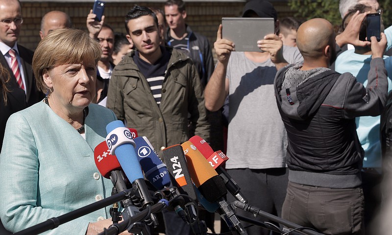 
              FILE - In this Sept. 10, 2015, file photo people take pictures as German Chancellor Angela Merkel, left, speaks during a statement as part of a visit at a registration center for migrants and refugees in Berlin, Germany. Germany marks a quarter-century as a reunited nation on Saturday, Oct. 3, 2015, with two leaders from the formerly communist east heading a country that increasingly asserts itself as Europe’s political heavyweight, and now faces a new challenge in a refugee influx that will demand deep reserves of resourcefulness and patience. (AP Photo/Michael Sohn, File)
            