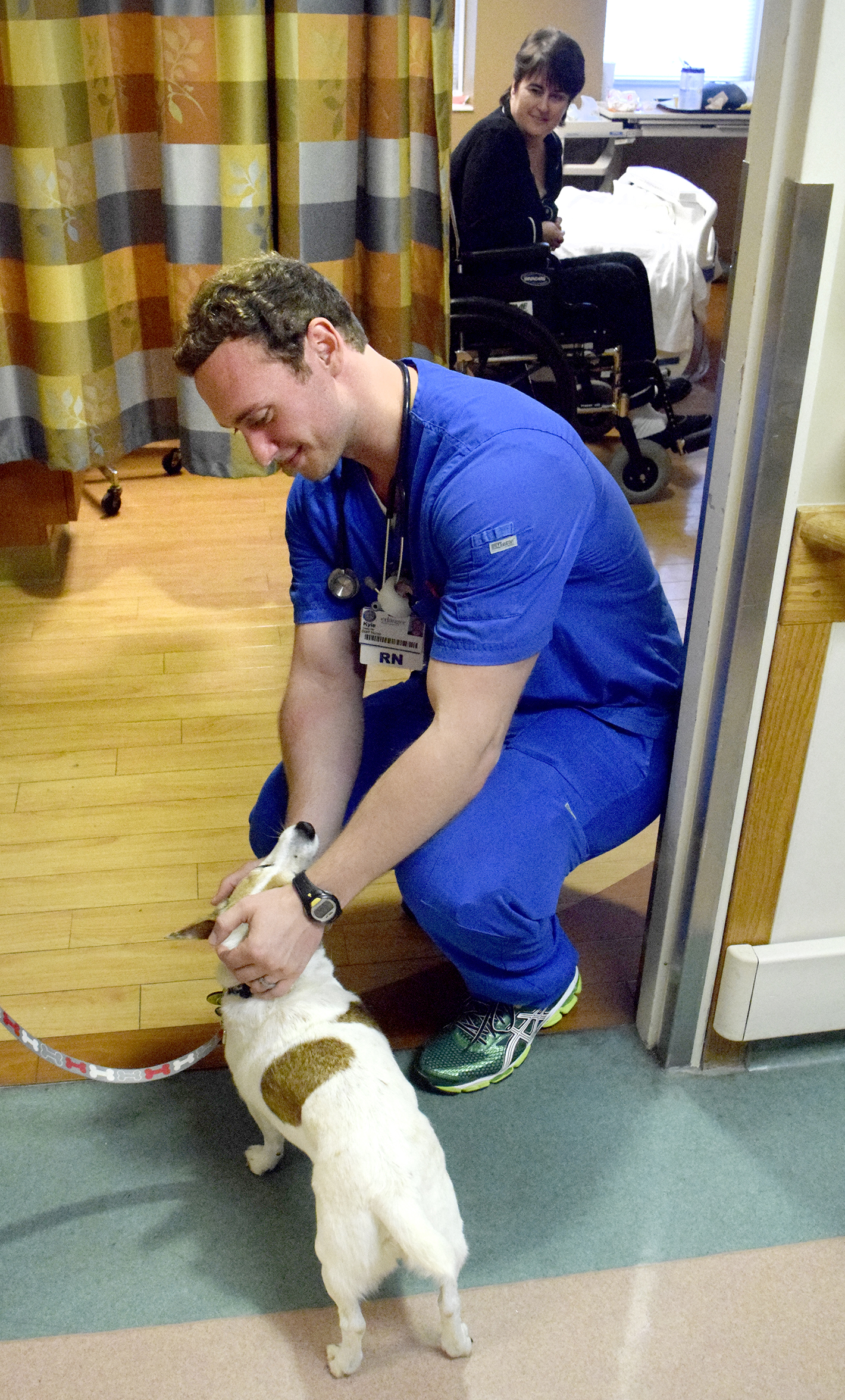 R.N. Kyle Casey pets Georgia, a 12-year old Jack Russell Terrier owned by Susan Millican, after the dog visited patient Edie Robinson (background). Erlanger Hospital is taking applications from dog owners for their pet to be a therapy dog.