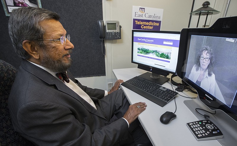 In this Tuesday, Aug. 18, 2015 photo provided by East Carolina University, Dr. Sy Saeed, chair of psychiatry and behavioral medicine at the Brody School of Medicine at East Carolina University, speaks to a colleague, Clinical Telehealth Manager Gloria Jones, during a routine test of the telepsychiatry system in Greenville, N.C. In vast swaths of America, patients face lengthy drives to reach the nearest psychiatrist, if they can even find one willing to see them. Some states are promoting wider use of long-distance telepsychiatry to fill the gaps in care.  (Cliff Hollis/East Carolina University via AP)