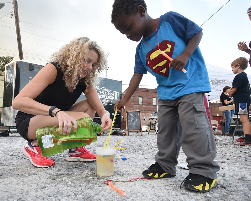 Leslie Morales, left, pours bubble fluid into a container for Theodore Sanders, 3, to dip in Tuesday on the lot at 1885 in St. Elmo during the National Night Out observation.