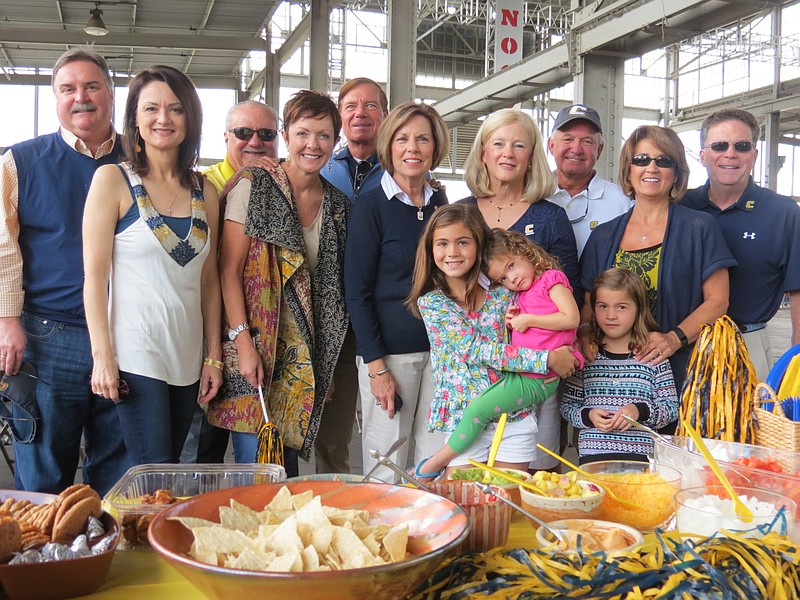 The UTC College of Business tailgaters set up a build-your-own taco buffet. Children in front are Laney Frost holding Molly Frost and Sally Frost. On the second row are Mary LeRoy, Kim White, Sue Culpepper, Claire Smith and Lisa Frost. In back are Scott LeRoy, Joe Dan White, Lee Culpepper, Roger Smith and Steve Frost.