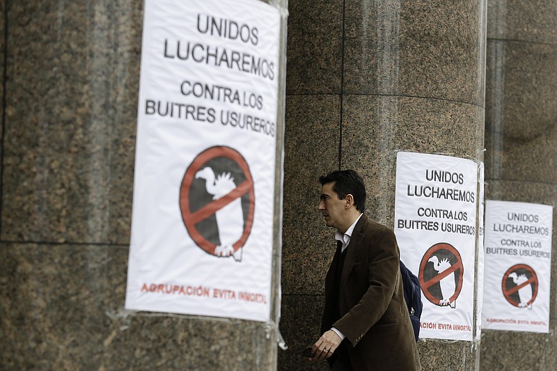 
              FILE - In this July 29, 2014, file photo, a man walks by signs posted at the entrance of the Argentine Economy Ministry reading in Spanish; "Together we will fight against the loan shark vultures," referring to an unresolved dispute over $1.5 billion in unpaid debts after its record $100 billion default in 2001, known locally as "vulture funds," in Buenos Aires, Argentina. Like a dark cloud, the bitter fight between Argentina and a group of holdout creditors in the U.S. has hung over South America’s second largest economy for years, preventing the country from accessing international credit market. (AP Photo/Victor R. Caivano,File)
            
