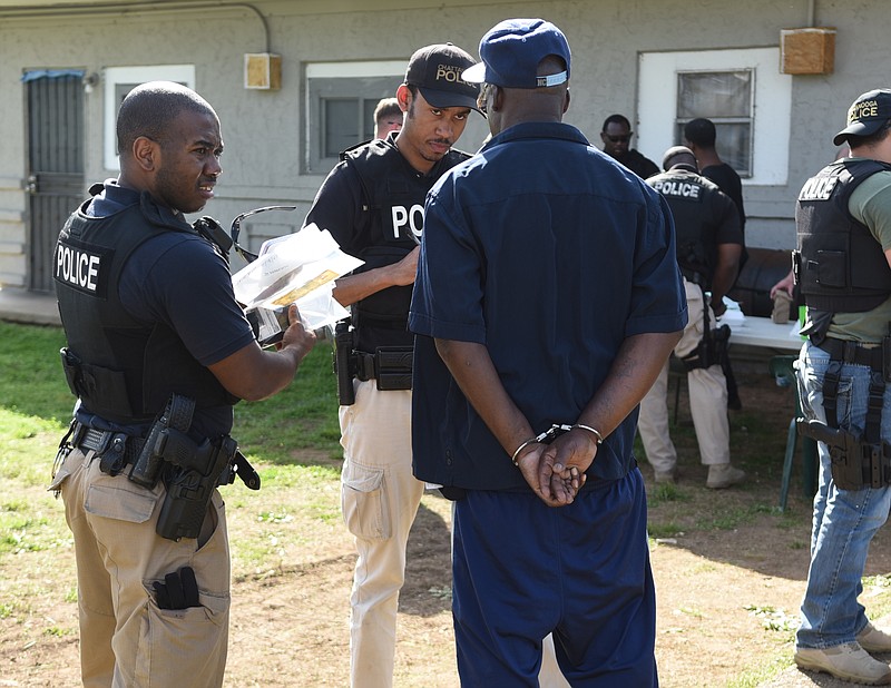 Chattanooga Police Department Street Crimes Response Team Investigators Cornelius Gaines, left, and Marc Saint Louis talk with Jerry Moore, seen in handcuffs after being arrested for allegedly selling crack cocaine to an undercover officer on Doris Street in this April 1, 2015, file photo. 