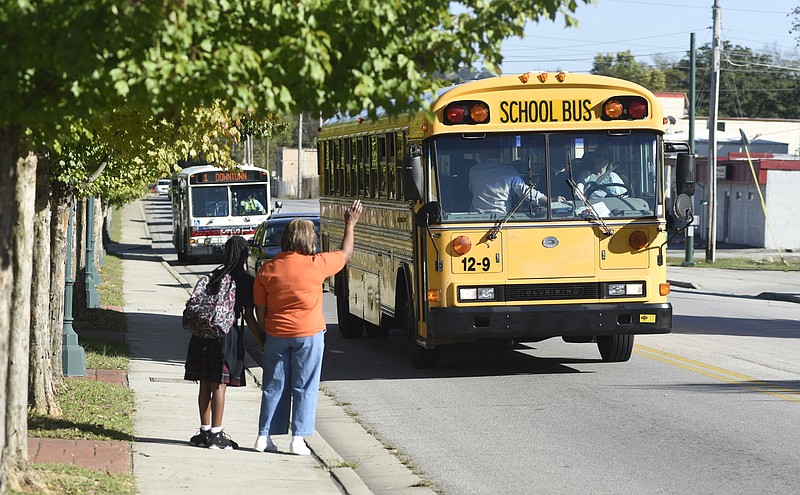 After meeting her school bus on 38th Street on Tuesday afternoon, Oct. 13, 2015, in Chattanooga, Tenn., Rosemary Porter, right, waves at the bus that dropped off her granddaughter, Jamaya Gantt, a student at the Chattanooga Charter School for Excellence. A shooting toward a group of students waiting for school buses happened near this spot on Tuesday morning. No one was wounded in the shooting that police believe is gang related. 