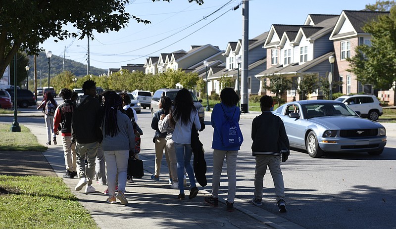 Howard students walk along 38th Street after arriving in a school bus on Tuesday afternoon, Oct. 13, 2015, in Chattanooga, Tenn. A shooting toward a group of students waiting for school buses happened near this spot on Tuesday morning. No one was wounded in the shooting that police believe is gang related. 