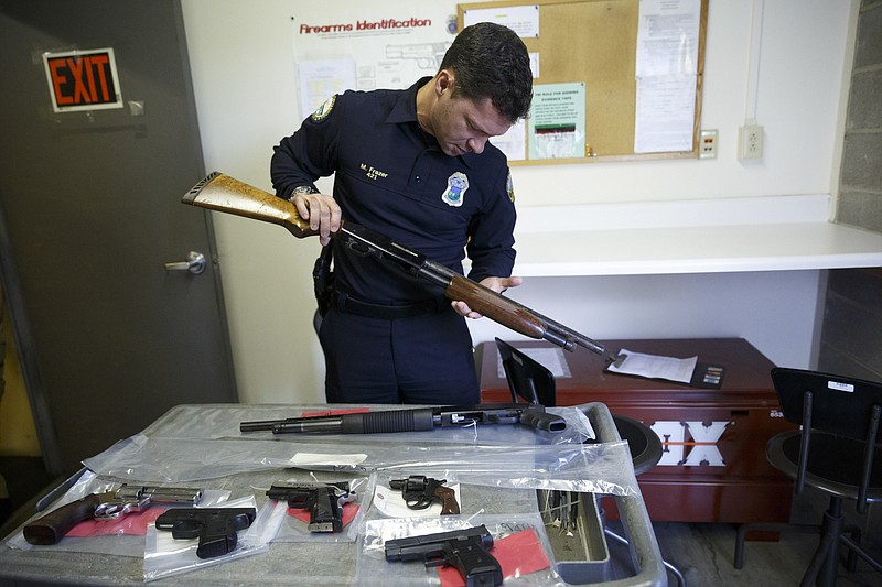 Chattanooga Public Information Officer Mark Frazer holds a seized 20-gauge shotgun next to a cart of other seized firearms. Police have seized an unusually large number of guns in only a few weeks.