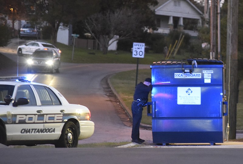 A Chattanooga Police Department officer looks in a dumpster near the scene of a shooting in the parking lot of the Family Dollar Store at the intersection of Wilcox Boulevard and Greenwood Road on Sunday, Nov. 22, 2015, in Chattanooga.