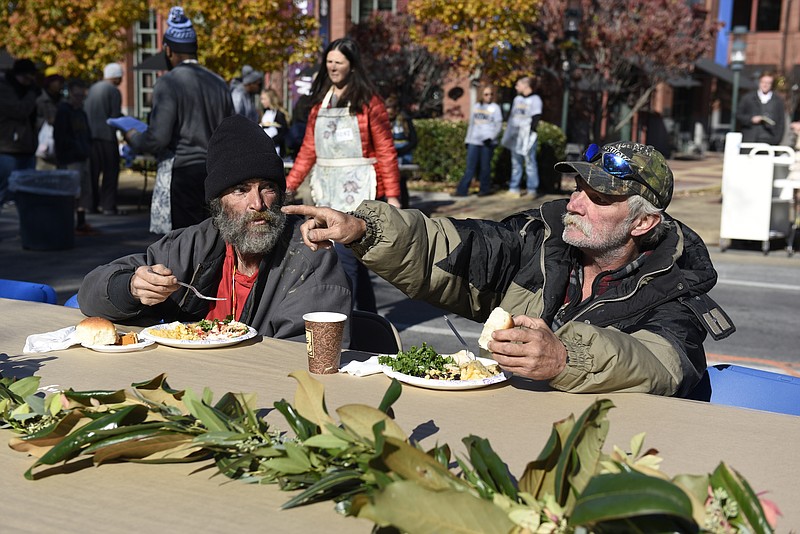 Randy Taylor, left, and Mark Pauley enjoy a free meal in the sunshine during the second annual One Table event Monday, Nov. 23, 2015, in Chattanooga, Tenn. The event features a Thanksgiving meal available to anyone, and is served on long table in the middle of ML King Boulevard in between Miller Park and Miller Plaza. 