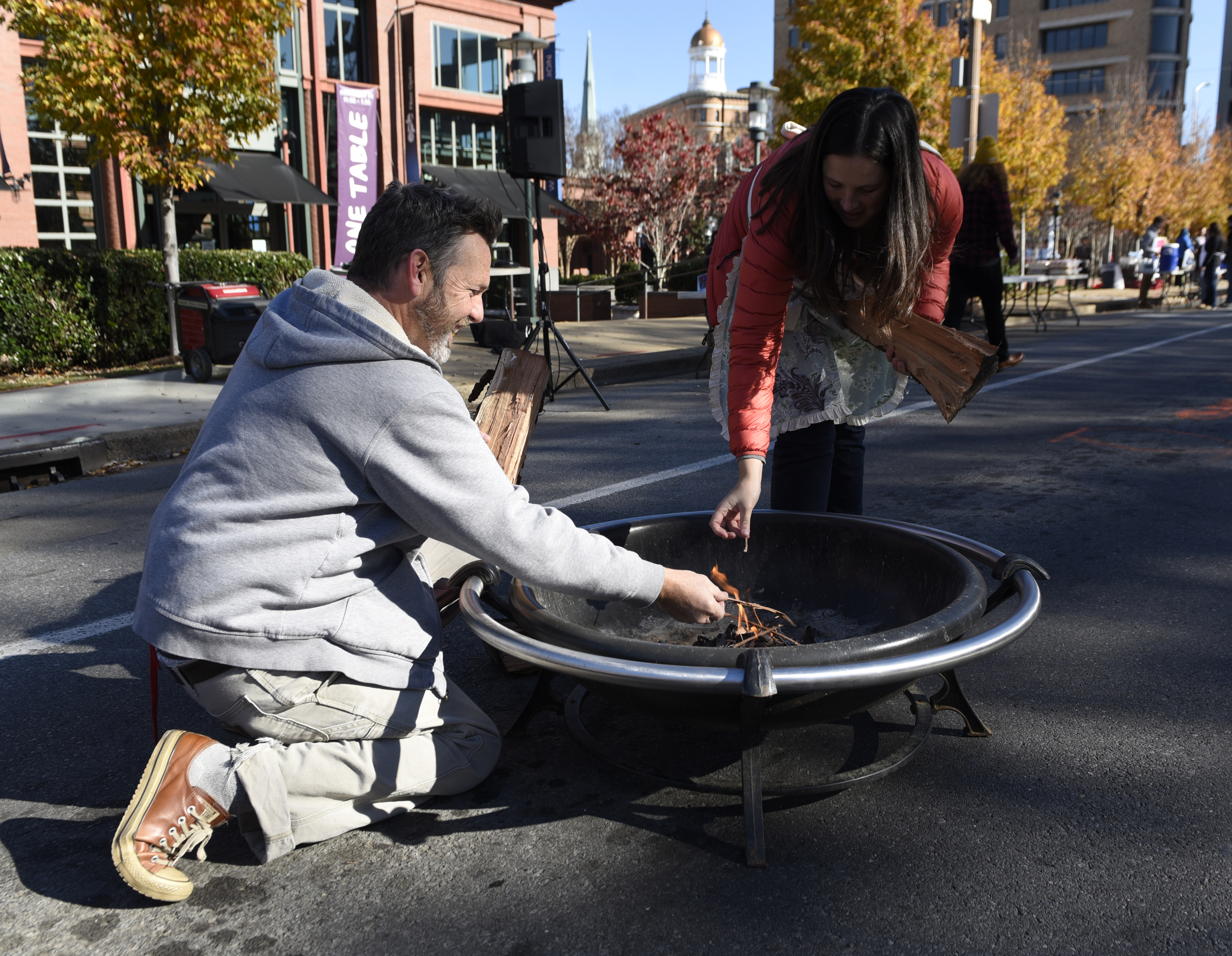 Kevin Bate, left, and Lori Quillen start a fire in one of four outdoor fireplaces in the street prior to the second annual One Table event Monday, Nov. 23, 2015, in Chattanooga, Tenn. The event features a Thanksgiving meal available to anyone, and is served on long table in the middle of ML King Boulevard in between Miller Park and Miller Plaza.
