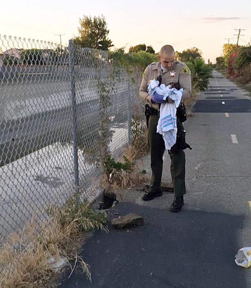 
              This Friday, Nov. 27, 2015 photo, provided by the Los Angeles County Sheriff's Department shows an unidentified deputy holding an infant girl where she was found abandoned under asphalt and rubble, left, near a bike path in Compton, Calif., as they seek the public's help in identifying her. The baby girl, who was wrapped in a blanket, was believed to be only less than a week old when two deputies found her Friday afternoon. She was taken to a hospital, where she is listed in stable condition. (Los Angeles County Sheriff's Department via AP)
            