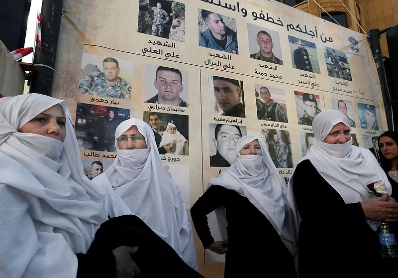 
              Lebanese Druze women stand next to posters with pictures of soldiers and policemen who were kidnapped by militants from the Islamic State group and al-Qaida's branch in Syria, the Nusra Front, in front of tents set up for a protest in downtown Beirut, Lebanon, Tuesday, Dec. 1, 2015. Syria's al-Qaida branch was releasing on Tuesday a group of Lebanese soldiers and policemen held captive since August 2014 as part of a swap deal brokered by Qatar that included Lebanon setting free an unspecified number of prisoners wanted by the militant group. (AP Photo/Bilal Hussein)
            