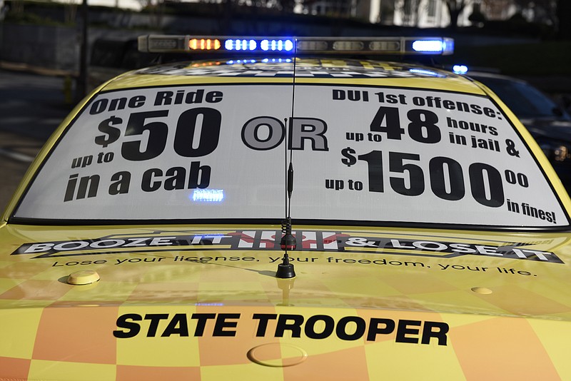 A sign comparing the costs of a taxi ride and a DUI conviction is seen on the back window of a Tennessee Highway Patrol vehicle painted to resemble a taxi during a news conference with members of the Chattanooga Police Department, Hamilton County Sheriff's Office and Georgia State Patrol on Monday, Dec. 7, 2015, in Chattanooga, Tenn., discussing DUI enforcement efforts during the holiday season. 