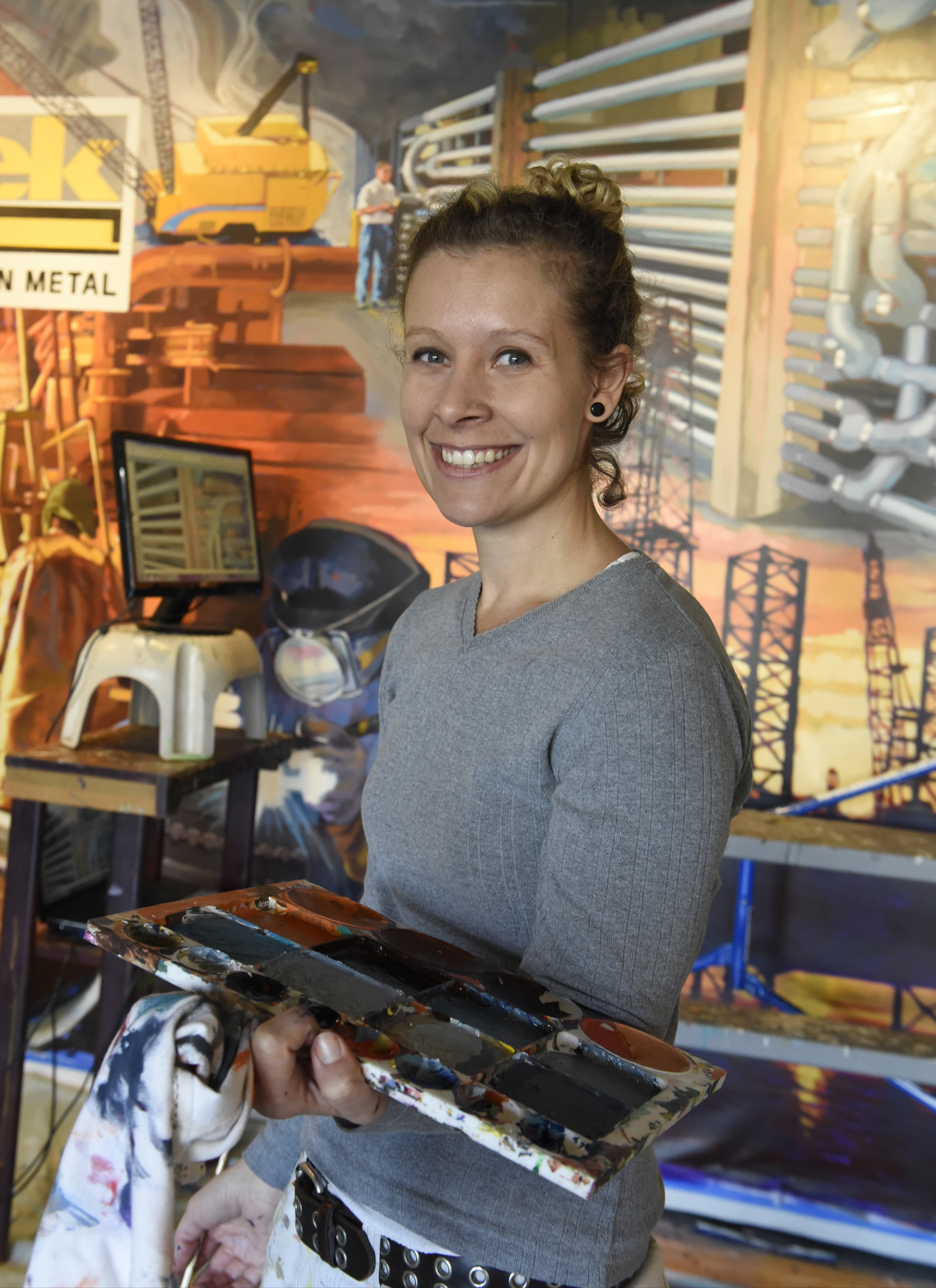 Ali Kay is photographed with one of her mural's in the lobby of the Chattanooga WorkSpace building on Thursday, Nov. 19, 2015, in Chattanooga, Tenn. This mural, eight feet tall and 21 feet wide, is one of eight of her murals that will be displayed in offices of MetalTek around the country.