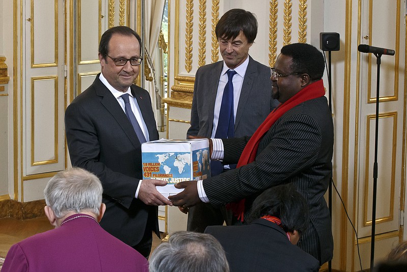 Cameroon's Augustine Njamnshi of the Pan African Climate Justice Alliance, right, hands over to France's President Francois Hollande, left, a box containing an international petition to support the climate talks while French environmentalist Nicolas Hulot stands between at the Elysee Palace in Paris, Thursday, Dec. 10, 2015. France's President Francois Hollande met religious figures lobbying against climate change on the side line of the COP21, United Nations Climate Change Conference in Le Bourget. (AP Photo/Michel Euler, Pool)