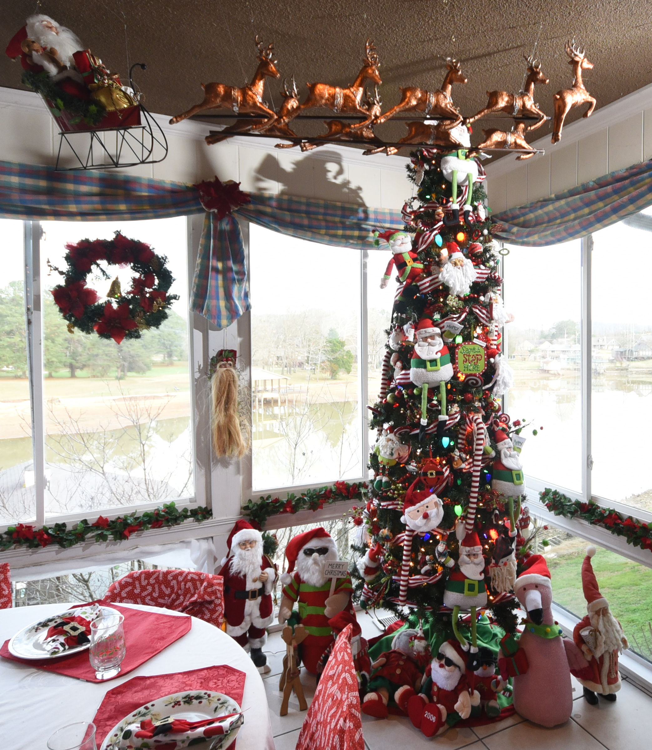 Katie Myers' collection of 300 Santas decorate the sunroom. She made the Santa and sleigh pulled by resin reindeer that is suspended from the ceiling. Poinsettia garland outlines windows overlooking a branch of Savannah Bay.