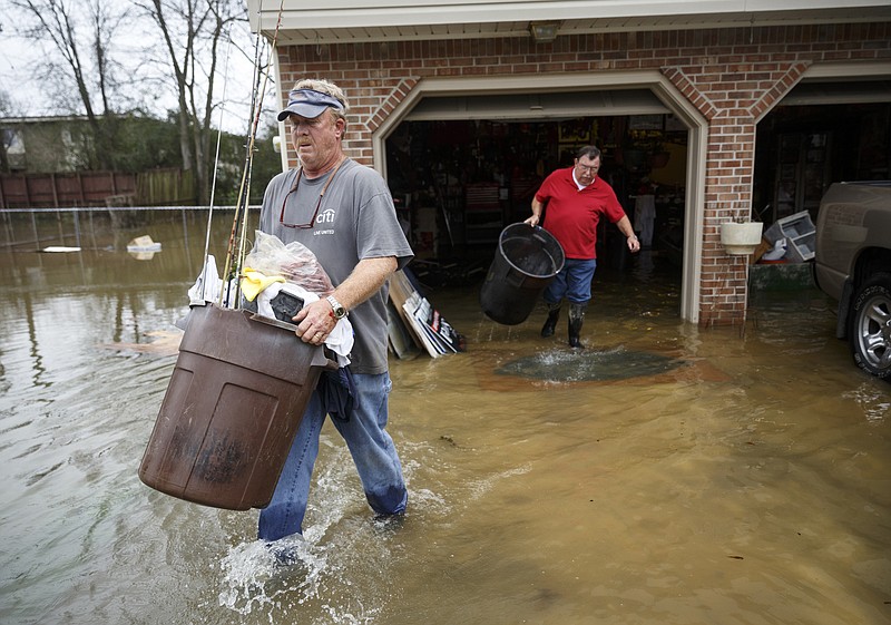 Rex Wheeler, left, and his neighbor Charlie Snyder carry trash cans filled with items out of Wheeler's flooded basement after heavy rains brought flooding to the region Saturday, Dec. 26, 2015, in East Ridge, Tenn. Rain is expected to continue into the next week.