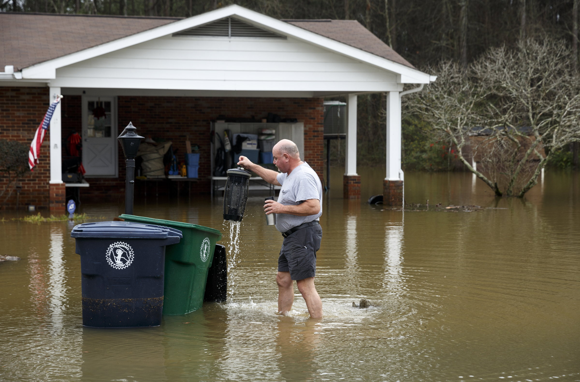 A man rights trash cans in front of a home on Spring Valley Drive after Christmas day rainfall brought South Chickamauga Creek to a flood stage of about 26.5 feet on Sunday, Dec. 27, 2015, in East Ridge, Tenn. Major flood stage classification for the creek is 27 feet.