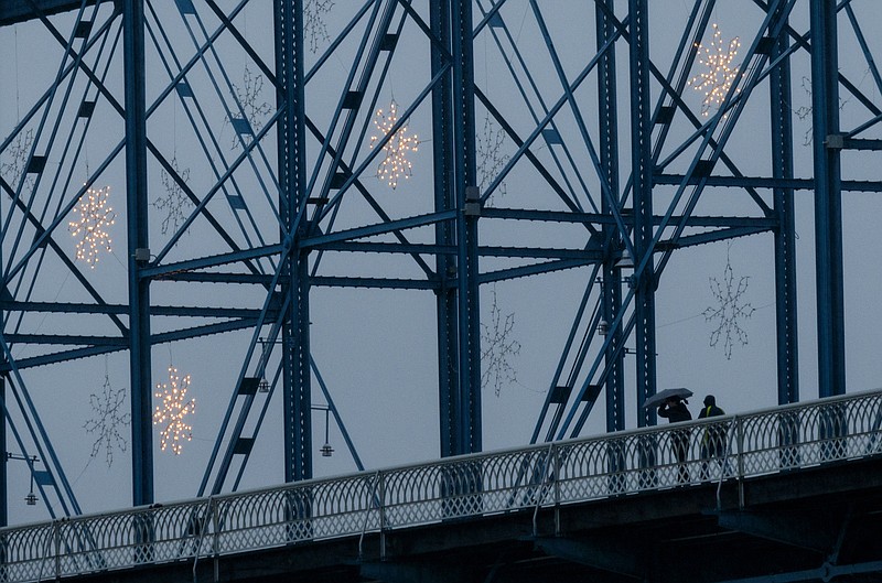 Pedestrians walk along the Walnut Street Bridge during afternoon rainfall after additional storms swept through the region Monday, Dec. 28, 2015, in Chattanooga, Tenn. The region recorded record-high temperatures over the past week amid heavy rainfall.