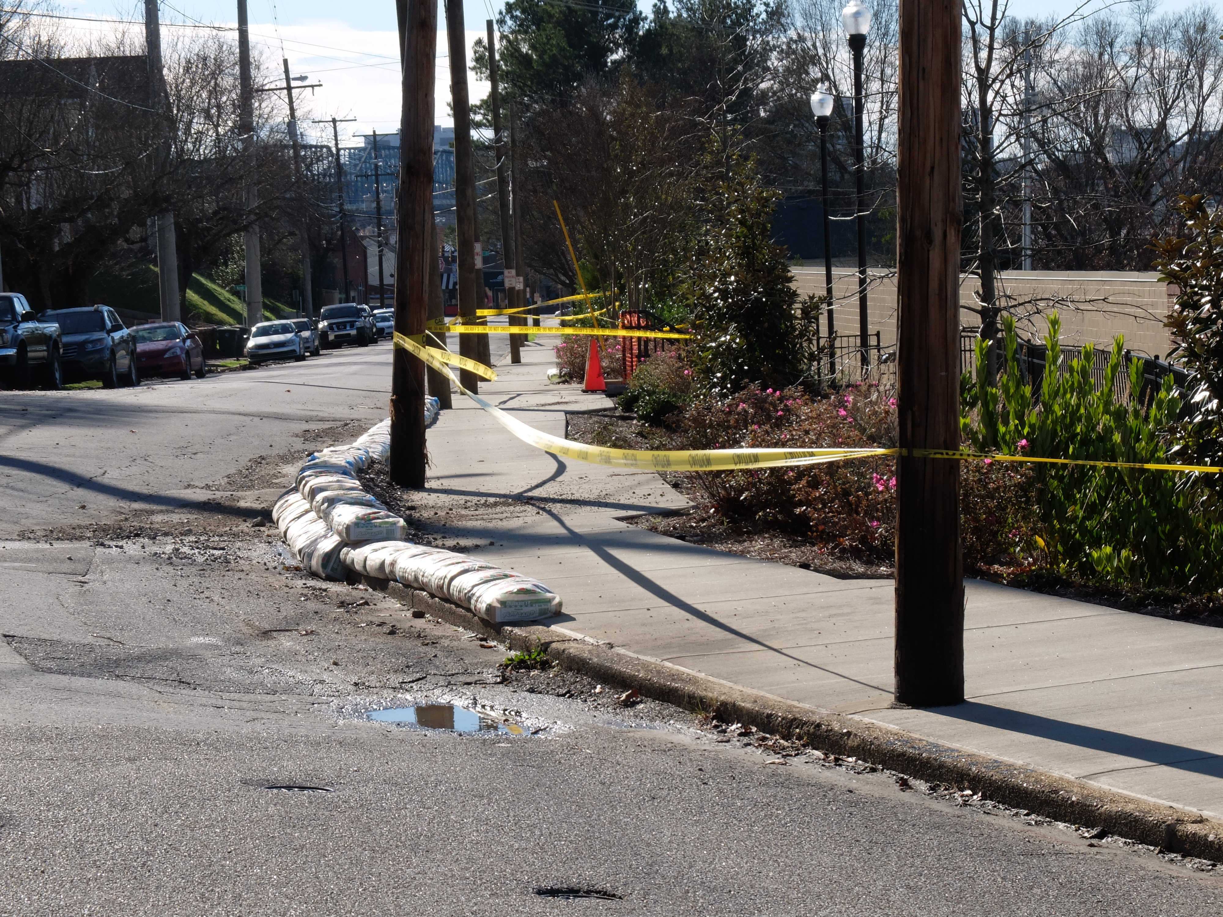 Yellow caution tape blocks the sidewalk and sand bags have been placed in the roadway along Woodland and Hamilton Avenues. The retaining wall on the east side of the Publix parking lot is suspected of moving as a result of recent heavy rains.
