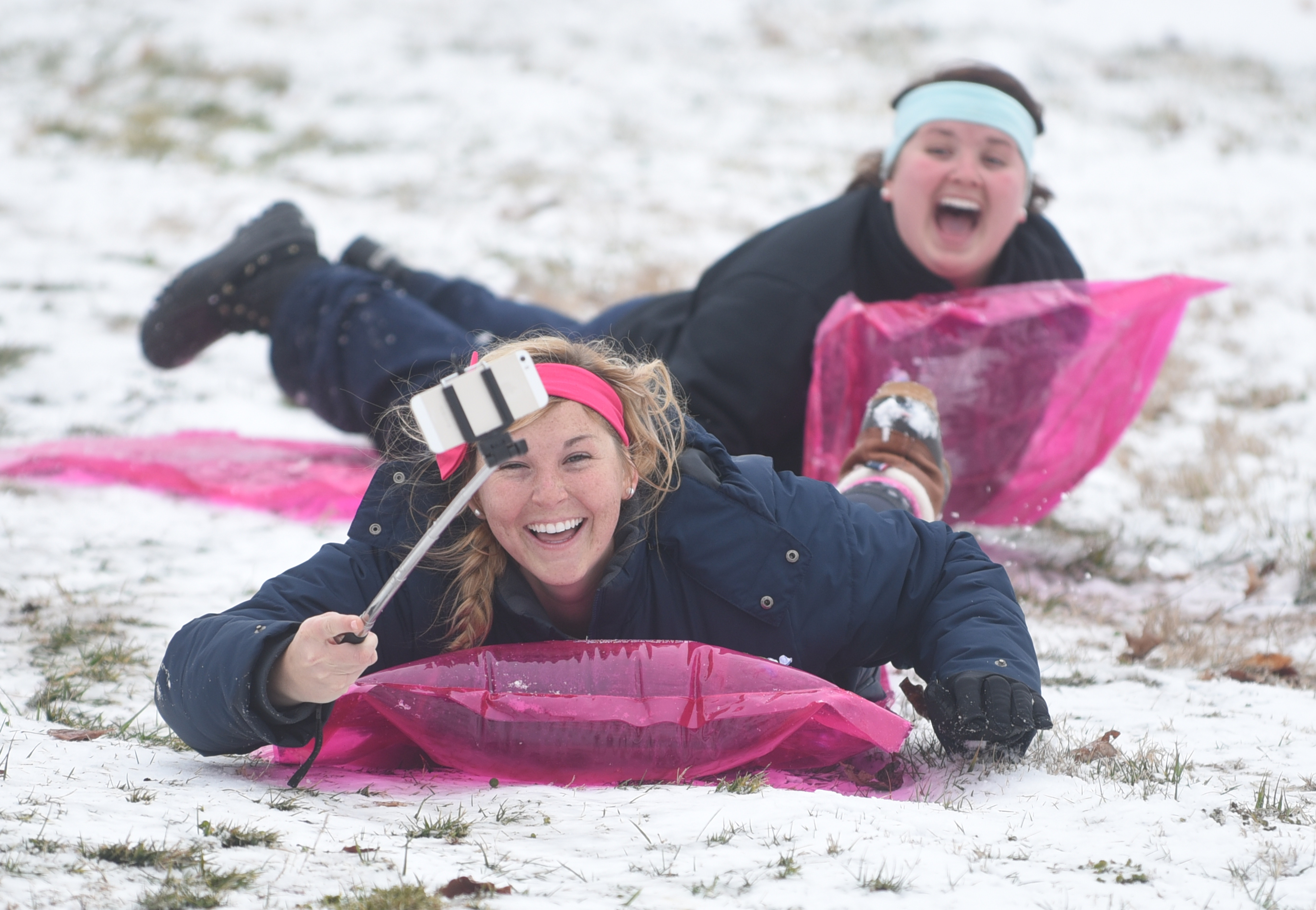 Katie Deems, front, holds her phone out to shoot video as she and Jessa Watts slide on pool floats down a hill near Lee University in Cleveland, Tenn., on Feb. 24.