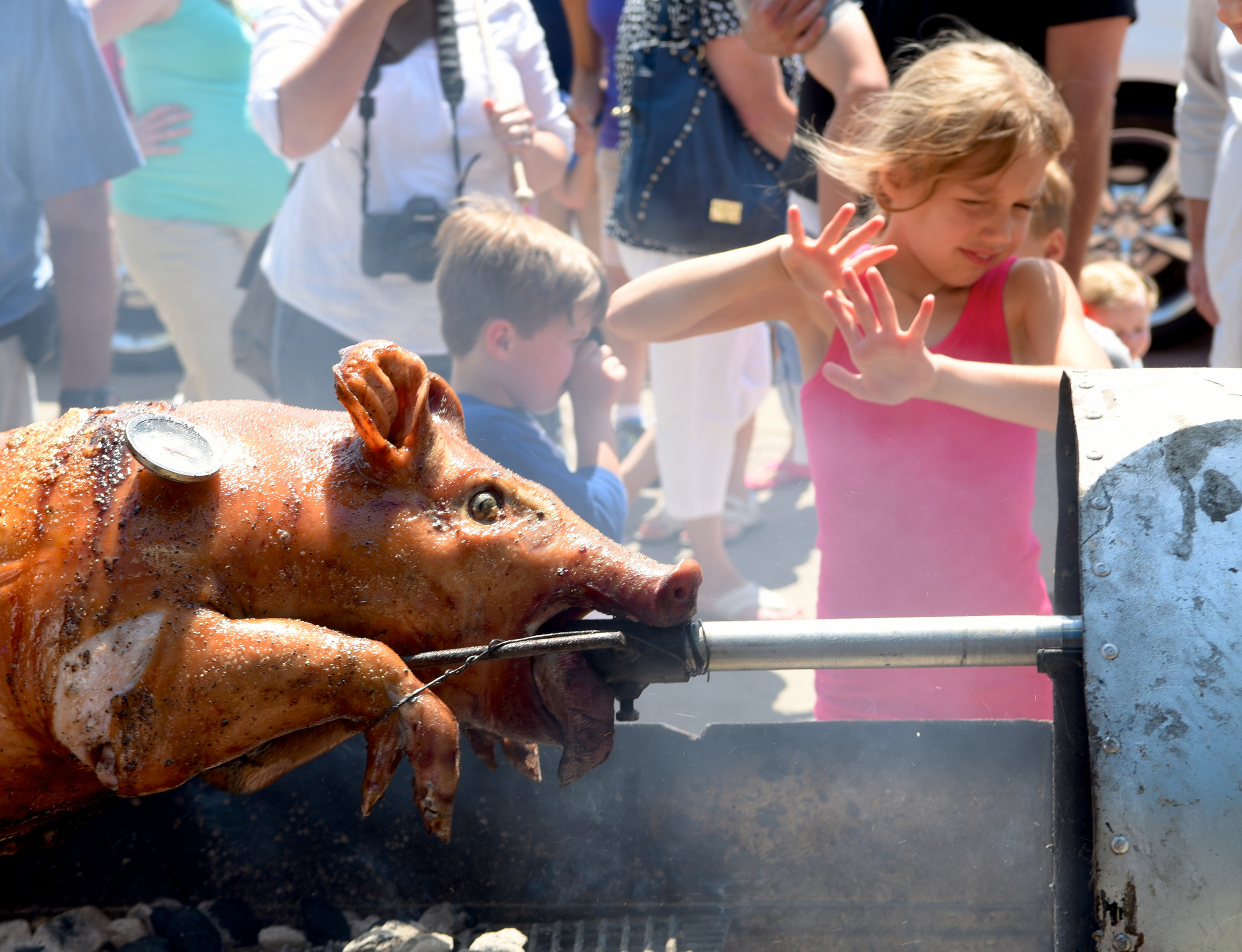 Gracen Rawlinson tries to shield herself from the smoke as she watches a roasting pig turn on a spit during the Beast Feast BBQ Festival on May 24 at the Chattanooga Market.