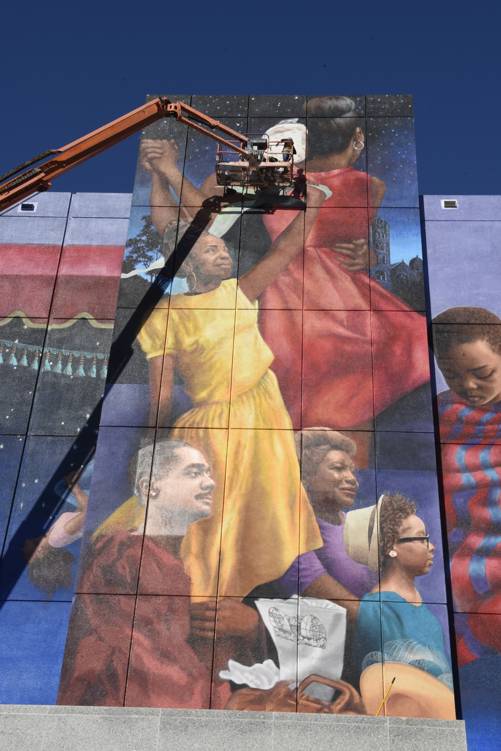 Hollie Berry and Hannah Hahn use a 120-foot lift truck to add the face of Bessie Smith as they and others work on a giant mural on the side of the AT&T building on Martin Luther King Boulevard.