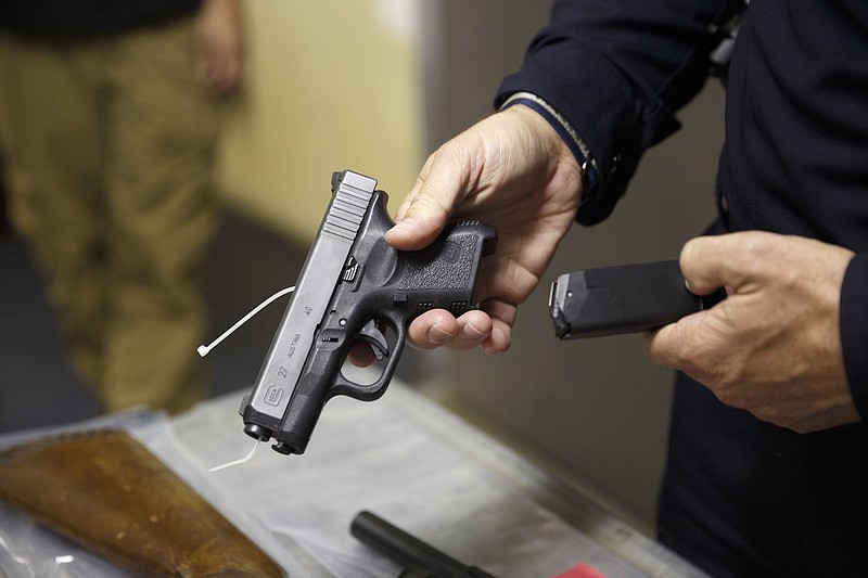 Staff photo by Doug Strickland / Chattanooga Police Public Information Officer Mark Frazer holds a seized handgun next to a cart of other seized firearms in the lobby of the property evidence room at the Police Services Center last October. Police said in the fall that they had seized an unusually large number of illegally possessed guns in a matter of only a few weeks.