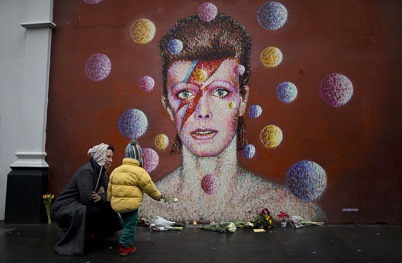 
              A woman and child place a flower alongside other tributes beside a mural of British singer David Bowie by artist Jimmy C in Brixton, south London, Monday, Jan. 11, 2016. David Bowie, the iconic and shape-shifting British singer whose illustrious career lasted five decade with hits like "Fame," ''Heroes" and "Let's Dance," died Sunday after a battle with cancer. He was 69. The singer, who was born David Jones at the family home in the Brixton area of London, came of age in the glam rock era of the early 1970s. (AP Photo/Matt Dunham)
            